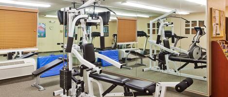 A gym with various exercise machines, a mirrored wall, and a blue mat on the floor.