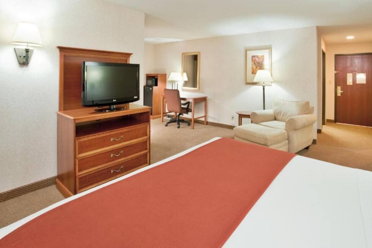 A hotel room with a bed, a television, a desk, a chair, a lamp, and a door.