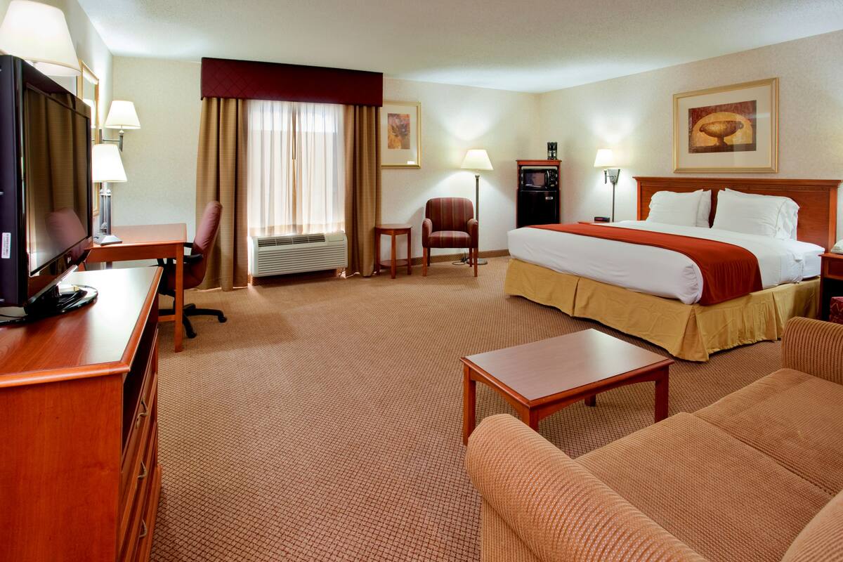 A hotel room with a bed, a desk with a TV, a chair, a small table, and a couch.