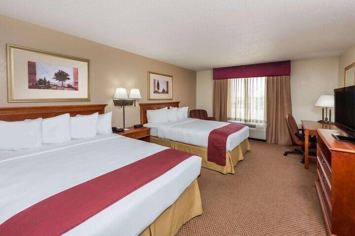 A hotel room with two beds, a desk, a television, and a window with curtains.