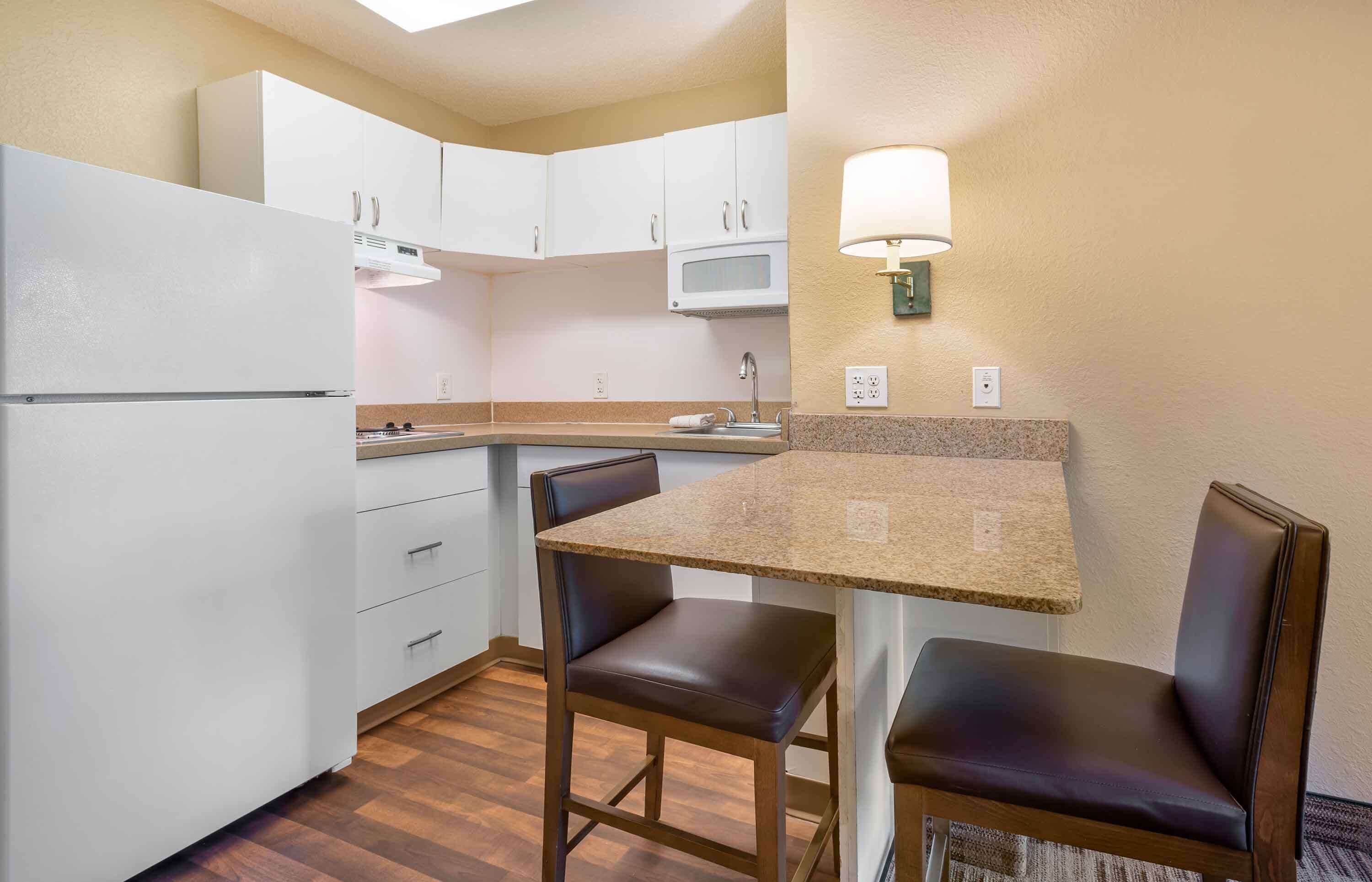 A compact kitchen with white cabinets, a microwave, a sink, and a table with two chairs.