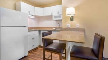 A compact kitchen with white cabinets, a microwave, a sink, and a table with two chairs.