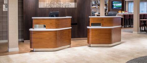 A reception area with two wooden reception desks, a digital screen, and a bar area with seating.