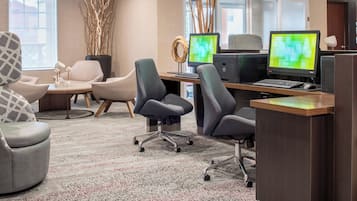 Un espacio de oficina moderno con varios puestos de trabajo, sillas ergonómicas, un amplio ventanal y elementos decorativos como un jarrón con ramas.