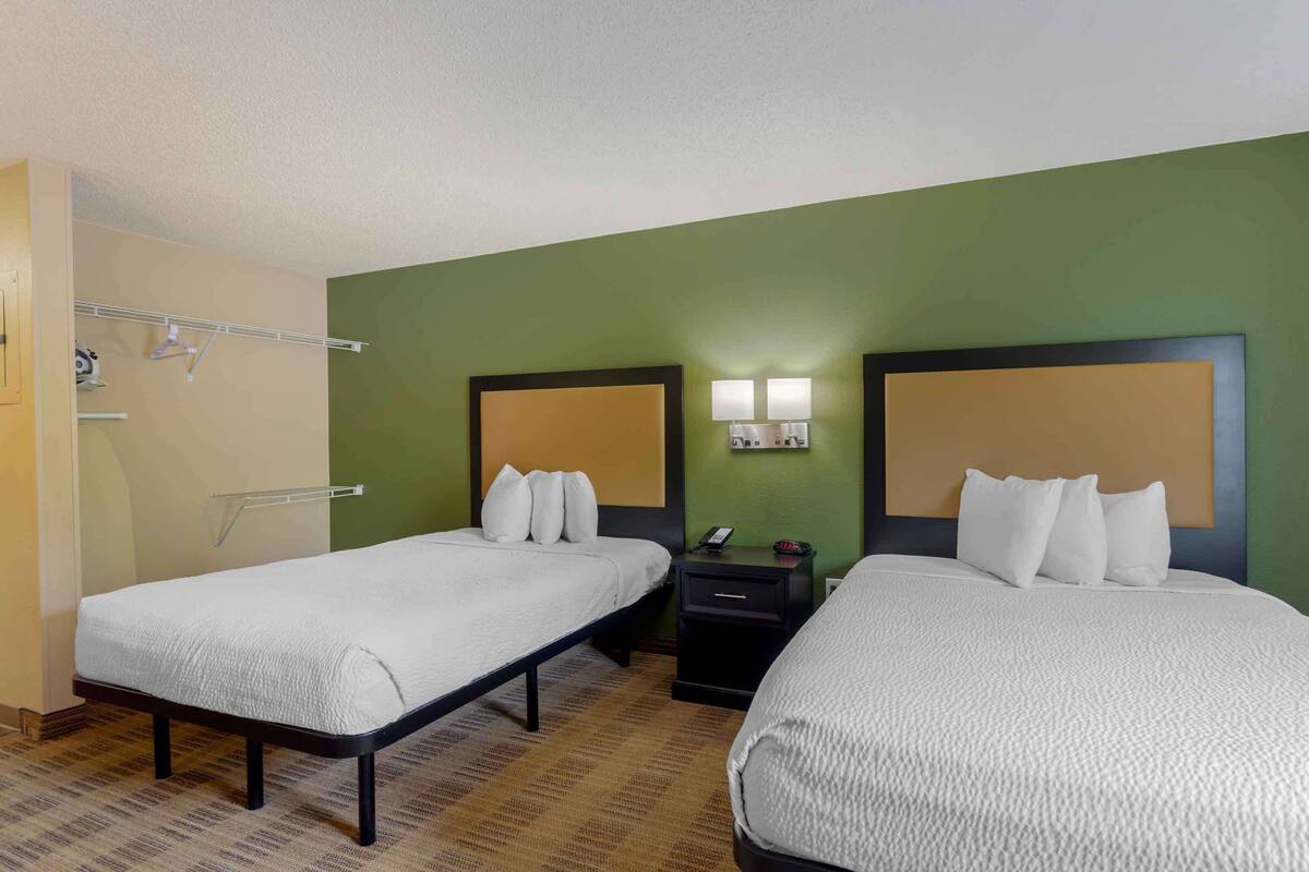 A hotel room with two beds, a nightstand, a wall-mounted light, and a towel rack.
