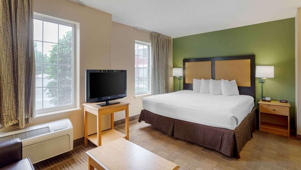 A hotel room with a large bed, a TV on a small table, a heater, and a nightstand with a lamp. - Extended Stay America Suites Memphis Germantown (Memphis)