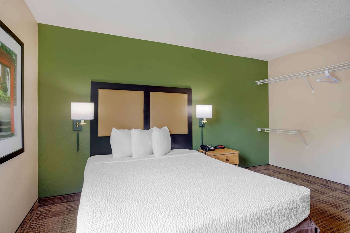 A hotel room with a large bed, two bedside lamps, a nightstand with a phone, and a wall-mounted drying rack.