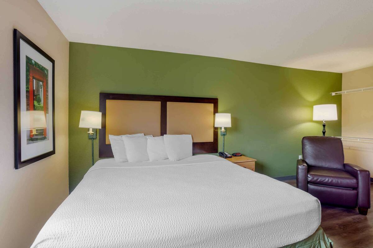 A hotel room with a large bed, two bedside lamps, a chair, and a framed picture on the wall.