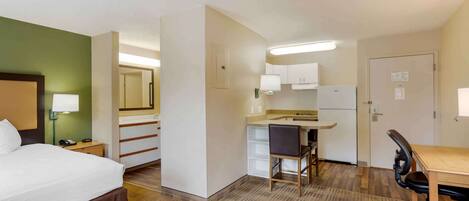 Habitación de hotel con cama, escritorio, silla, kitchenette pequeña y baño.