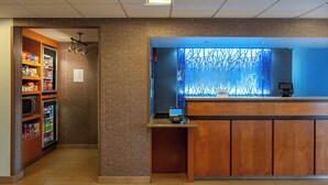 Zona de recepció d'hotel amb un taulell de fusta, una pantalla digital i una màquina expenedora.