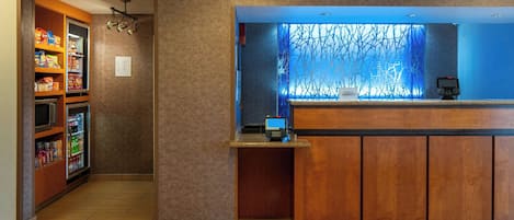 A hotel reception area with a wooden reception desk, a digital screen, and a vending machine.