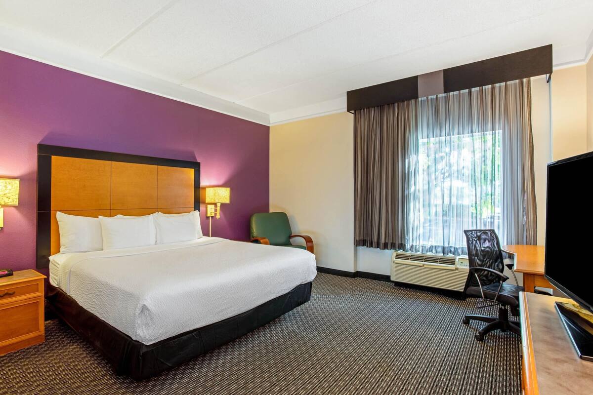 Une chambre d’hôtel avec un grand lit, un bureau doté d’un téléviseur à écran plat, une chaise et un appareil de climatisation.