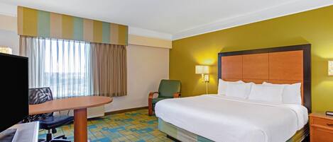 A hotel room with a large bed, a desk with a chair, a television, and a window with curtains.