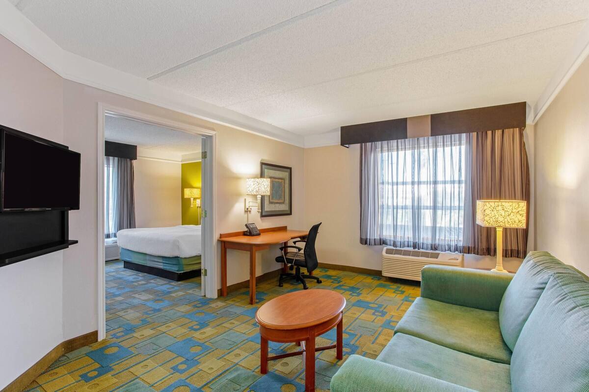 Une chambre d’hôtel avec un lit, un bureau, un canapé vert, une télévision et une fenêtre avec des rideaux.