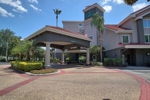 A hotel entrance with a covered waiting area, palm trees, and a clear blue sky.