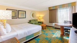 A hotel room with a bed, a green armchair, a small table, a desk with a chair, a TV, and a window with curtains. - La Quinta Inn & Suites by Wyndham Orlando I Drive/Conv Ctr (Orlando)