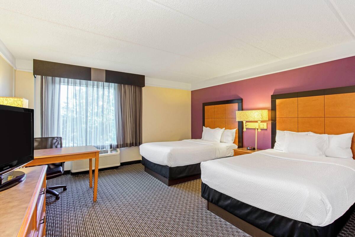 Une chambre d’hôtel avec deux lits, un bureau, une télévision et une fenêtre avec des rideaux.