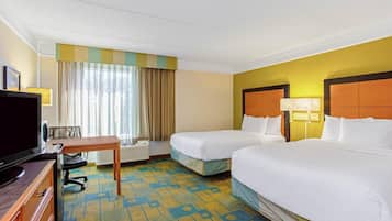 A hotel room with two beds, a desk with a chair, a television, and a window with curtains.