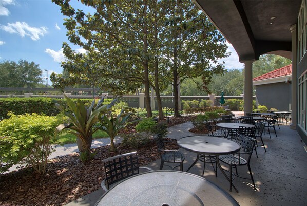 An outdoor patio area with tables and chairs, surrounded by trees and plants.