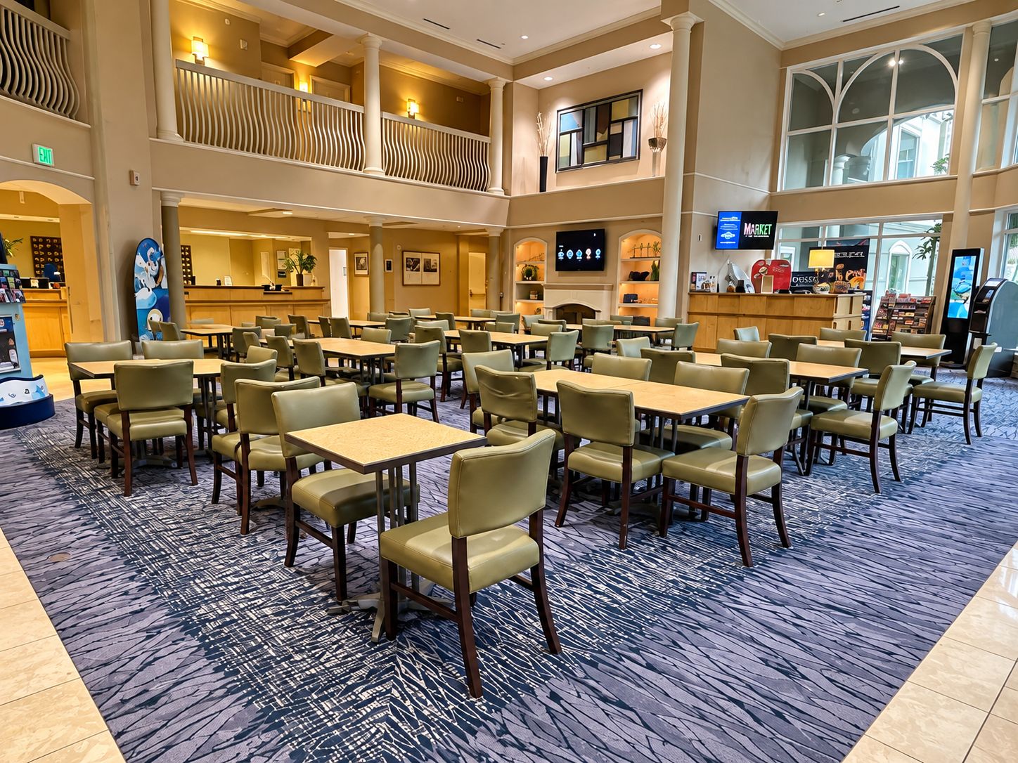 Een hotel lobby met meerdere eettafels en stoelen, een receptiebalie en een groot televisiescherm.