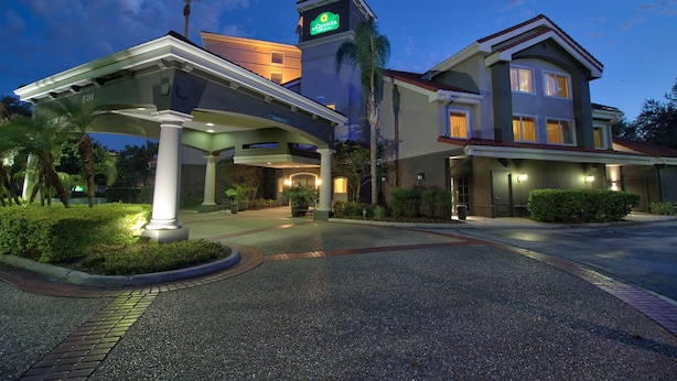 A hotel with a covered entrance, palm trees, and a sign indicating it is a Quinta hotel. - La Quinta Inn & Suites by Wyndham Orlando I Drive/Conv Ctr (Orlando)