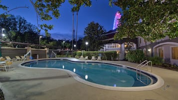 Una piscina con sillas de descanso y una noria al fondo.