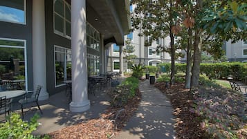 An outdoor patio area with tables and chairs, surrounded by trees and shrubs.