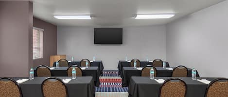 Sala de conferências com mesas, cadeiras, garrafas de água e uma televisão de tela plana.