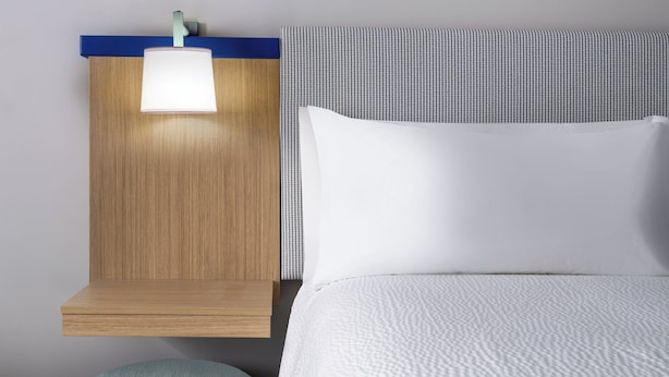 A neatly made bed with a white comforter and a headboard with a light fixture.