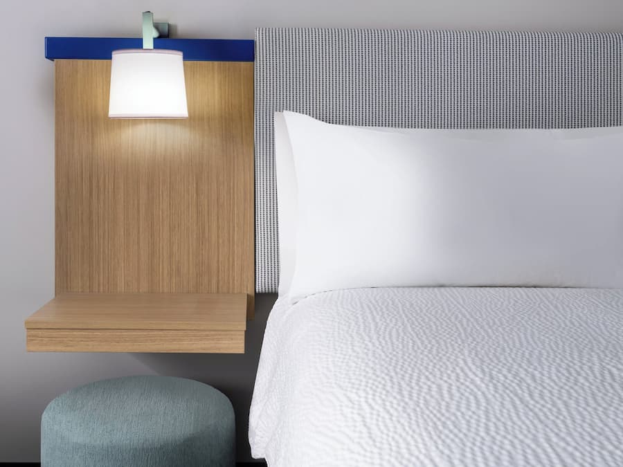 Una cama bien hecha con edredón blanco y cabecera con lámpara.