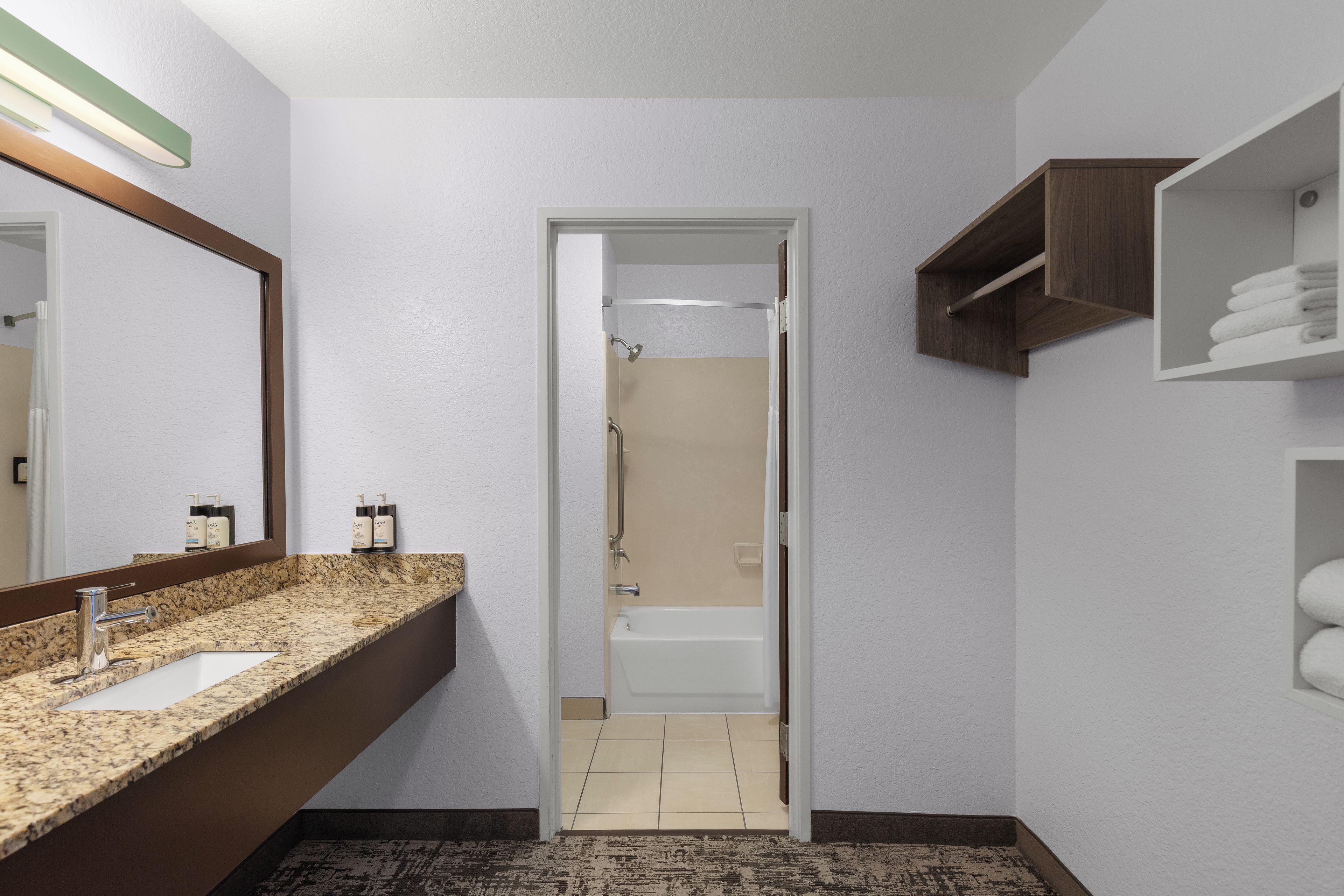 A bathroom with a granite countertop, a mirror, a shower, and a towel rack.