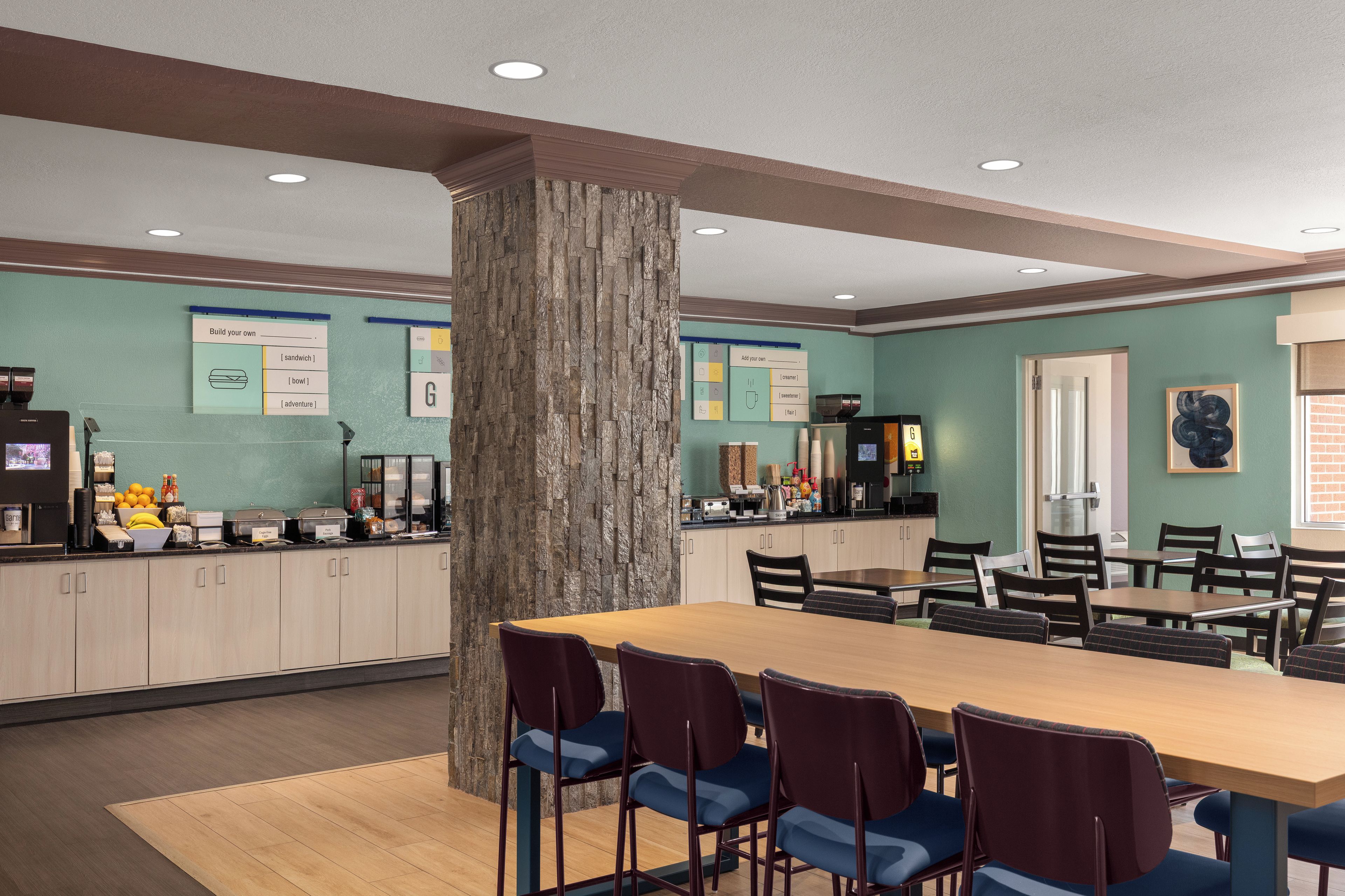 A dining area with a central column, tables, chairs, and a counter with various food items.