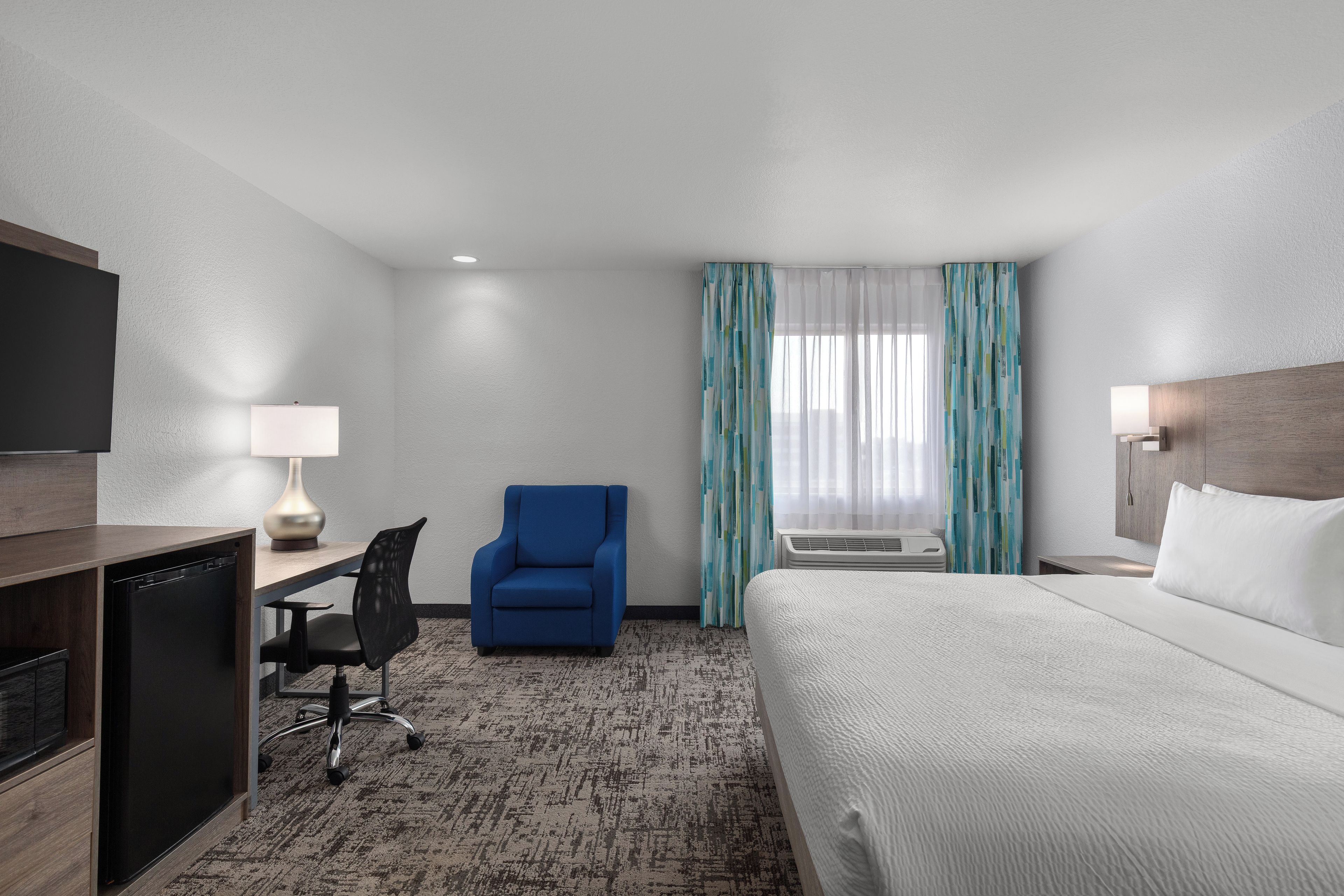 Una habitación de hotel con una cama, un escritorio con una silla, un televisor y una ventana con cortinas.