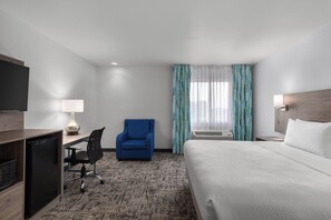 A hotel room with a bed, a desk with a chair, a television, and a window with curtains.