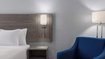 A hotel room with a bed, a nightstand, a lamp, and a blue armchair.
