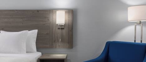 A hotel room with a bed, a nightstand, a lamp, and a blue armchair.