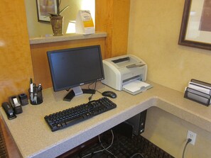 A desk with a computer monitor, keyboard, and printer. There are pens in a holder and a framed picture on the wall. - Garner Hotel Denver Airport Area by IHG (Denver)