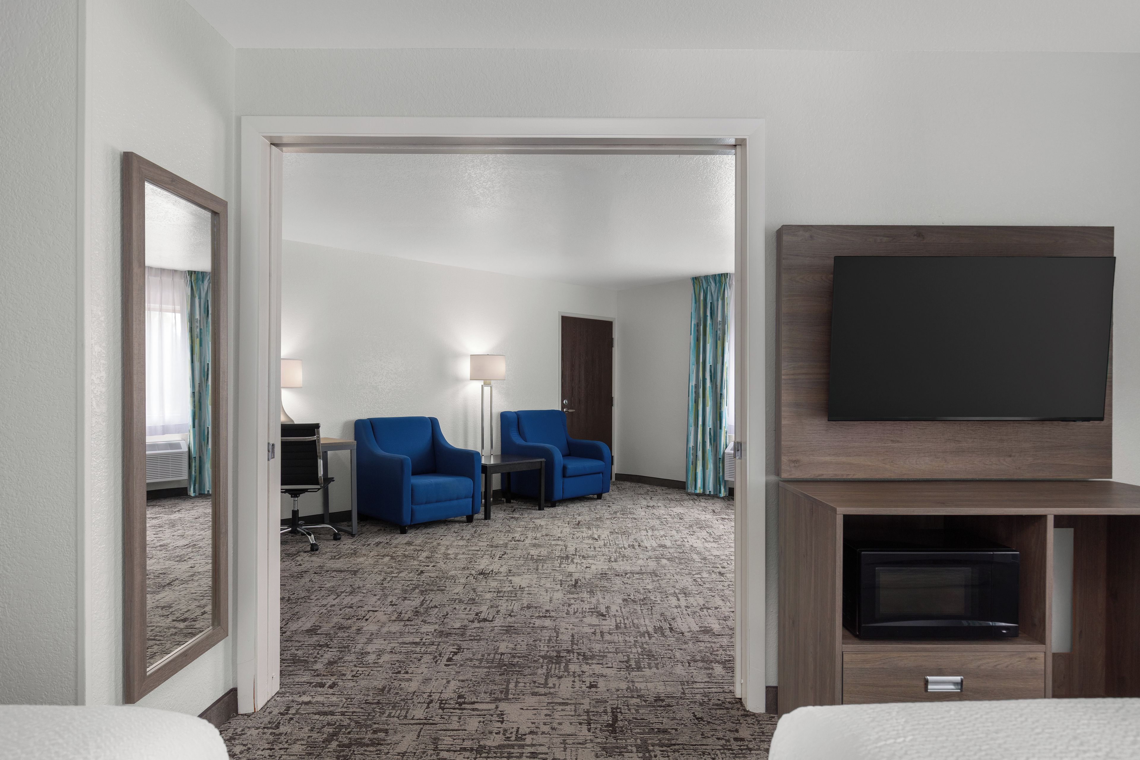 Habitación de hotel con televisor de pantalla plana, dos sillones azules, una mesita y piso alfombrado.