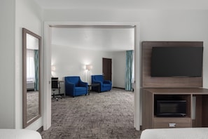Habitación de hotel con televisor de pantalla plana, dos sillones azules, una mesita y piso alfombrado.