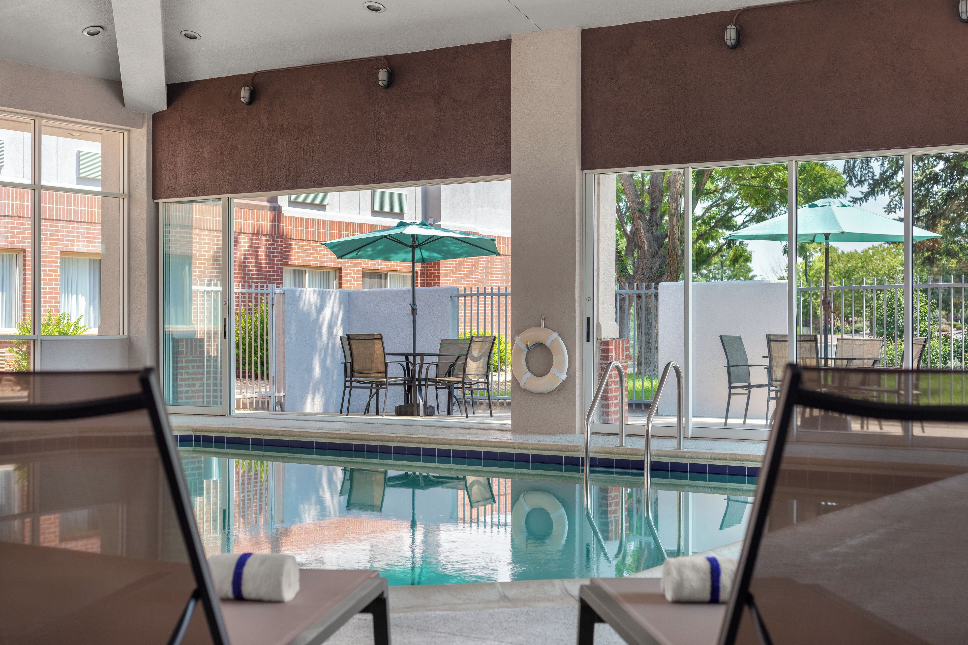 Uma área à beira da piscina com espreguiçadeiras, piscina e vista dos edifícios ao redor.