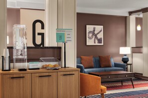 A hotel room with a wooden desk, a glass container, a sign with a letter 'G', a blue sofa, and a lamp. - Garner Hotel Denver Airport Area by IHG (Denver)