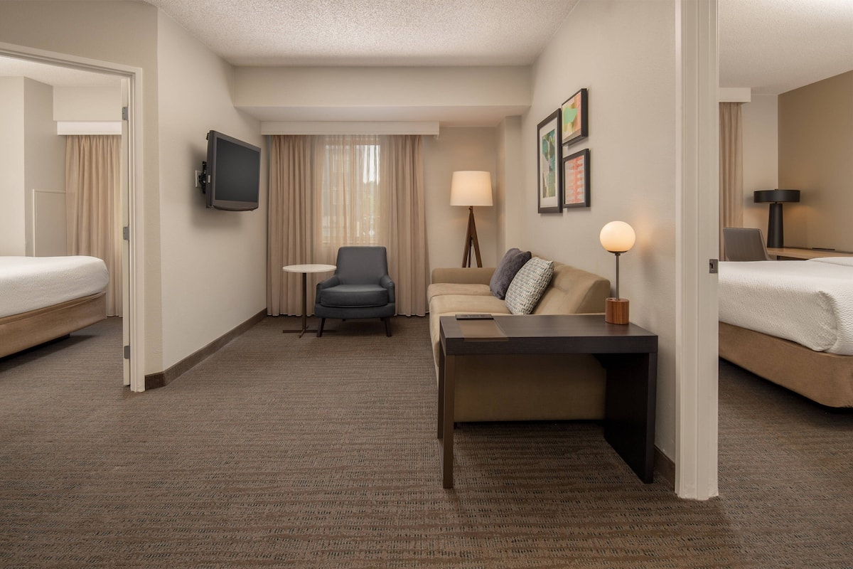 A hotel room with a bed, a sofa, a desk, a chair, a TV, and a lamp.