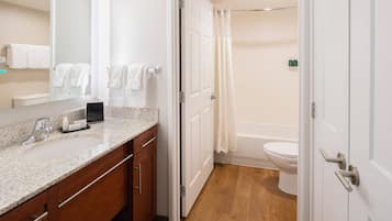 A modern bathroom with a granite countertop, wooden cabinets, a white sink, and a toilet.