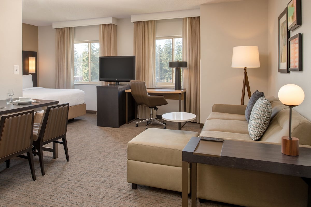 A hotel room with a bed, a desk, a chair, a sofa, and a TV.