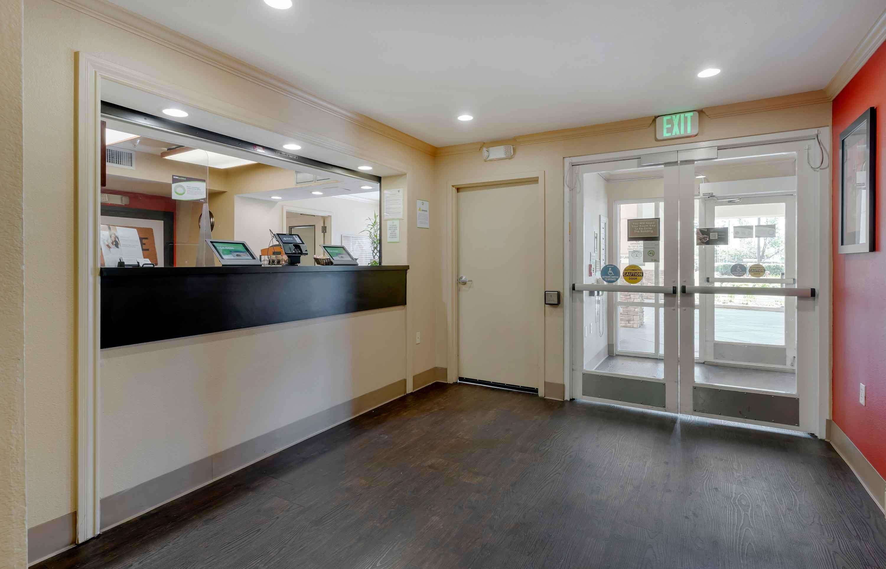 A hotel reception area with a reception desk, a glass door entrance, and an exit sign.