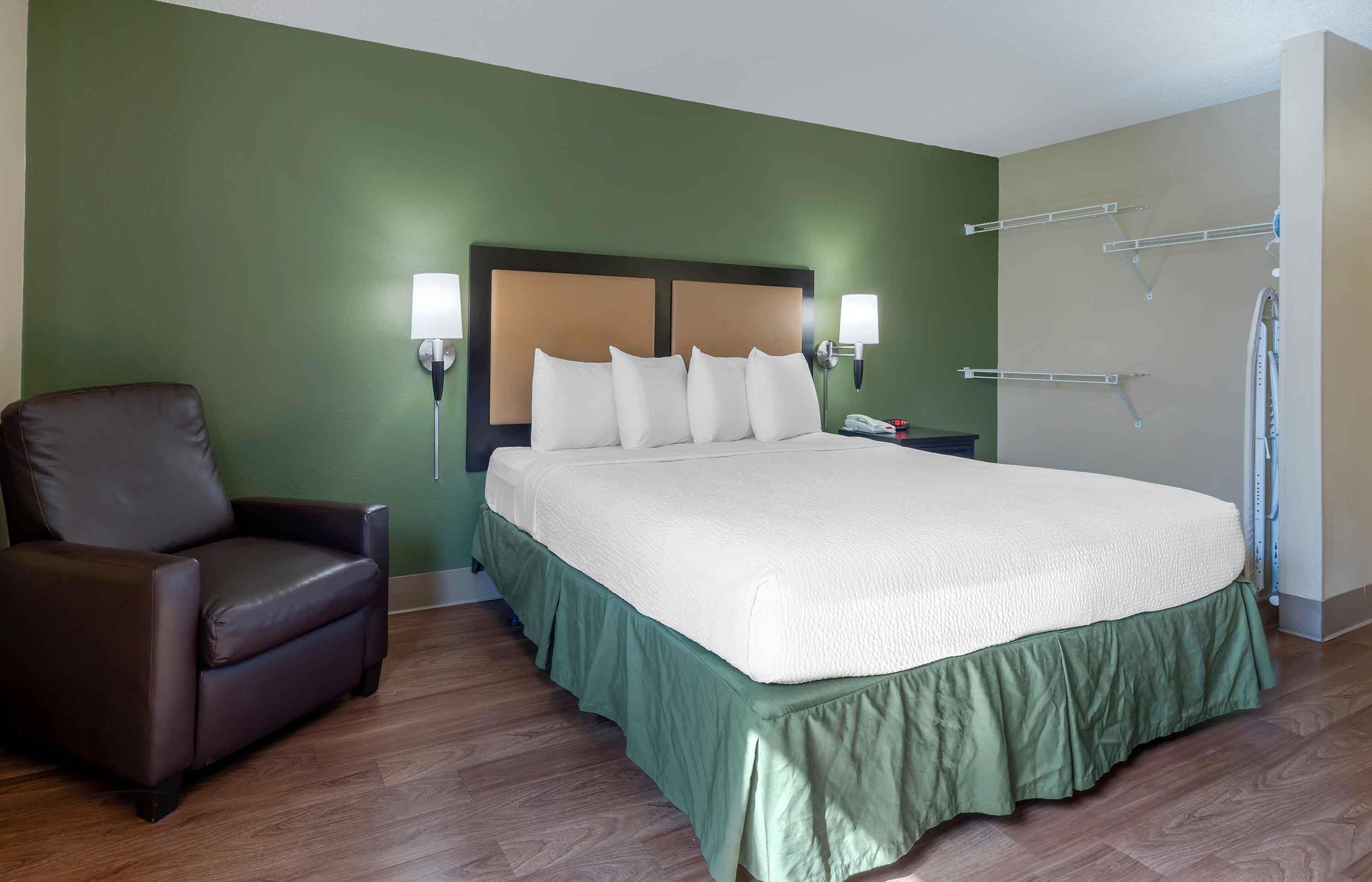A hotel room with a large bed, a brown leather chair, a green wall, and a white headboard.