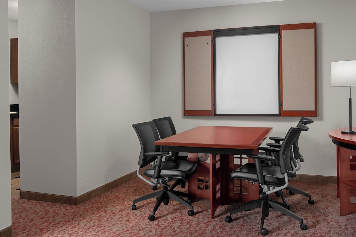 Un salón de conferencias con una mesa roja, sillas negras, una pizarra y una lámpara.