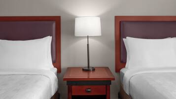 A hotel room with two beds, a nightstand, and a lamp.