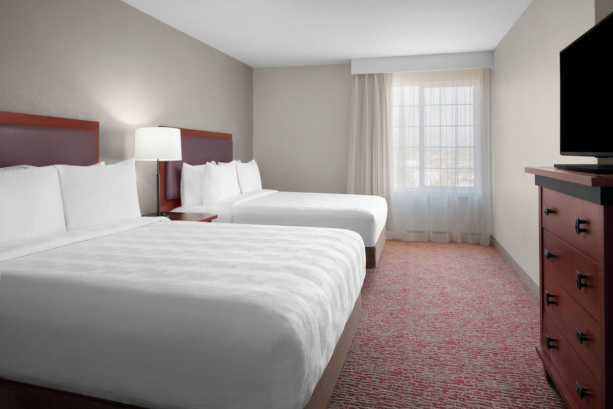 Habitación de hotel con dos camas, televisión, cómoda y ventana con cortinas.