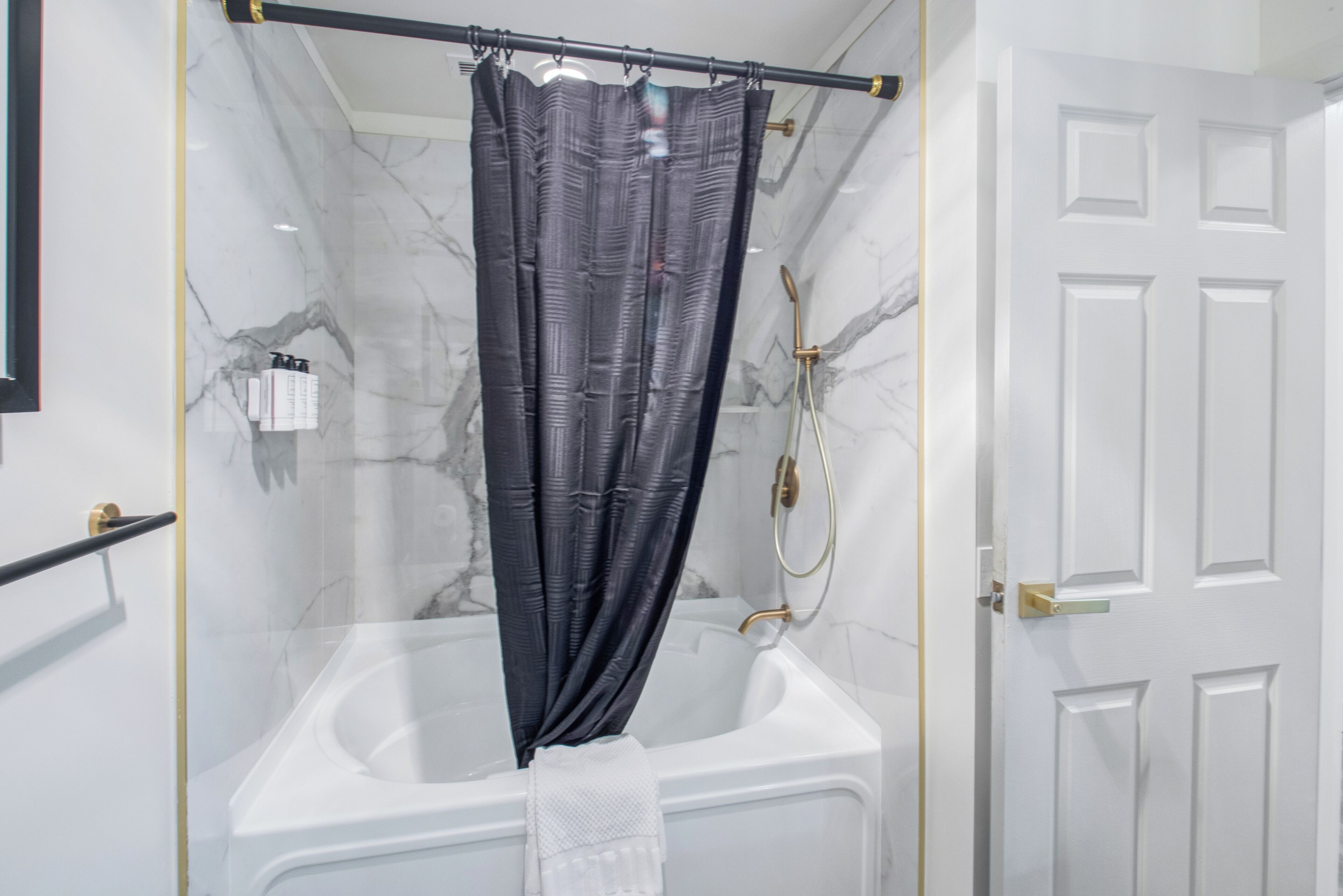 A modern bathroom with a glass-enclosed shower, a white bathtub, and a marble wall.
